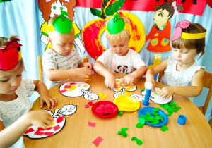 Dzieci za pomocą kolorowego papieru wyklejają jabłko.