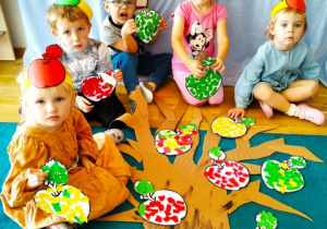 Dzieci układają wcześniej wykonane jabłka na papierowym drzewie.