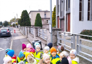 Dzieci stoją przy znaku drogowym, który informuje nas o przystanku autobusowym.