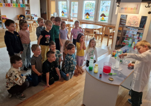 Dzieci obserwują co stanie się kiedy Olek doleje octu do wody z sodą oczyszczoną.