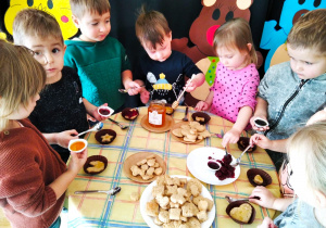 Dzieci dekorują ciasteczka miodkiem i dżemem.