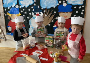 Dzieci prezentują produkty i przybory kuchenne potrzebne do zrobienia pierników.