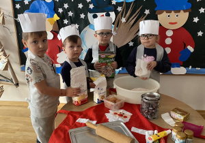 Dzieci wsypują mąkę i przyprawę do piernika do miski.