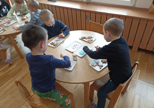 Dzieci przy drugim stoliku dekorują upieczone pierniczki.