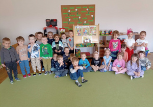 Wspólne zdjęcie przedszkolaków przy sztaludze z ilustracjami wielkanocnymi.