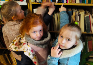Dziewczynki pokazują książki, które chciałyby wypożyczyć z biblioteki.