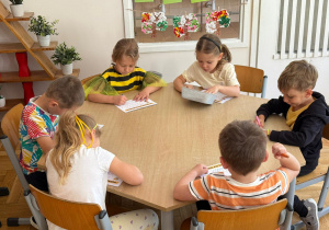 Dzieci wypełniają karty pracy i kolorują obrazki z pszczołami.