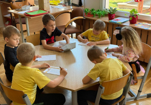 Dzieci wypełniają karty pracy i kolorują obrazki z pszczołami.