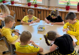 Dzieci wypełniają karty pracy i kolorują obrazki z pszczołami.