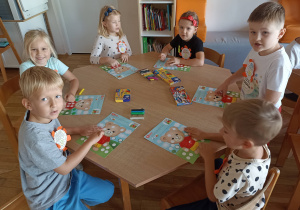 Przedszkolaki przy pierwszym stoliku wykonują pracę plastyczną „Miś z kropek”.