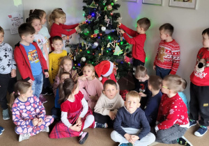 Dzieci ozdabiają choinkę w holu przedszkola.